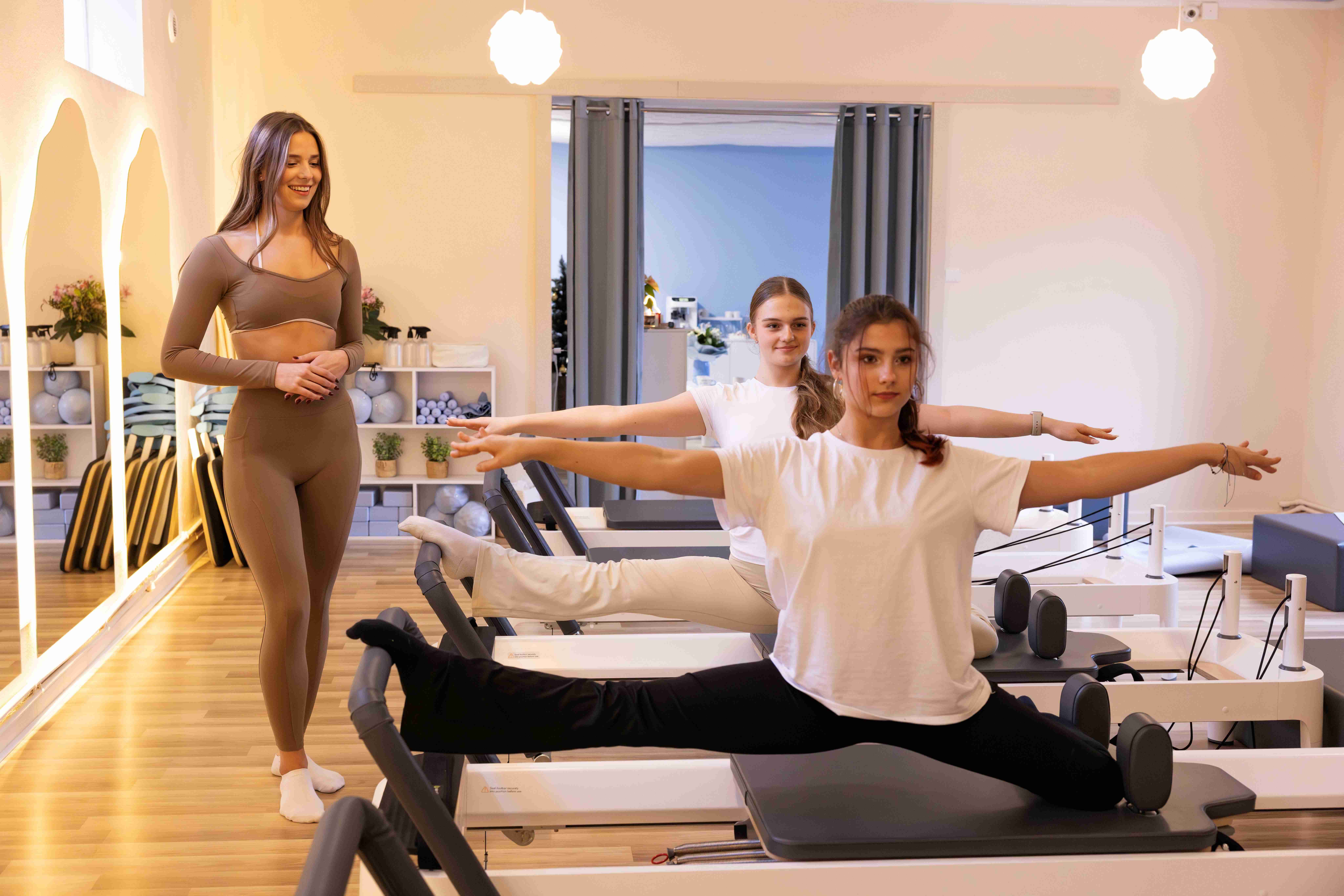 Dwie kobiety podczas wspólnego treningu pilates na reformerach w Nube Pilates Otwock - pod okiem instruktora.